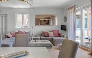Ein modernes Wohnzimmer mit einer Couch, Sesseln, einem Couchtisch, einem Fernseher und einem großen Fenster.