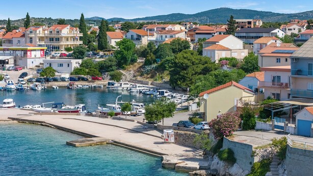Un port de plaisance situé sur la côte, avec des bateaux, un quai sablonneux et des immeubles résidentiels en arrière-plan.