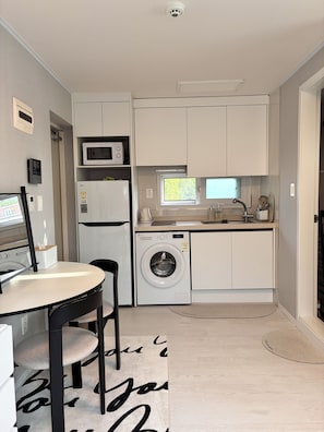 Une cuisine compacte équipée d’un lave-linge, d’un four à micro-ondes et d’un petit évier.