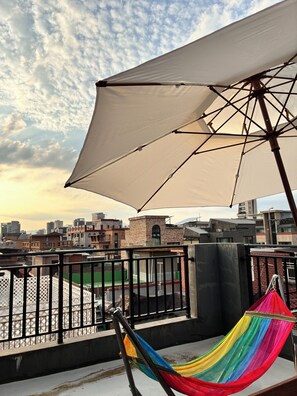 Una terraza en la azotea con una hamaca, un paraguas grande y vistas de la ciudad.