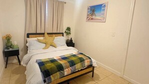 A bedroom with a bed, a ceiling fan, a nightstand, a window with curtains, and a wall-mounted picture. - 1 bedroom Private Studio with Patio. 5 Min to Hard Rock Stadium & Every Event. (Miami Gardens)