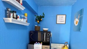 A kitchen with a blue wall, a microwave, a stove, and a refrigerator. There are shelves with kitchen items and a plant. - 1 bedroom Private Studio with Patio. 5 Min to Hard Rock Stadium & Every Event. (Miami Gardens)