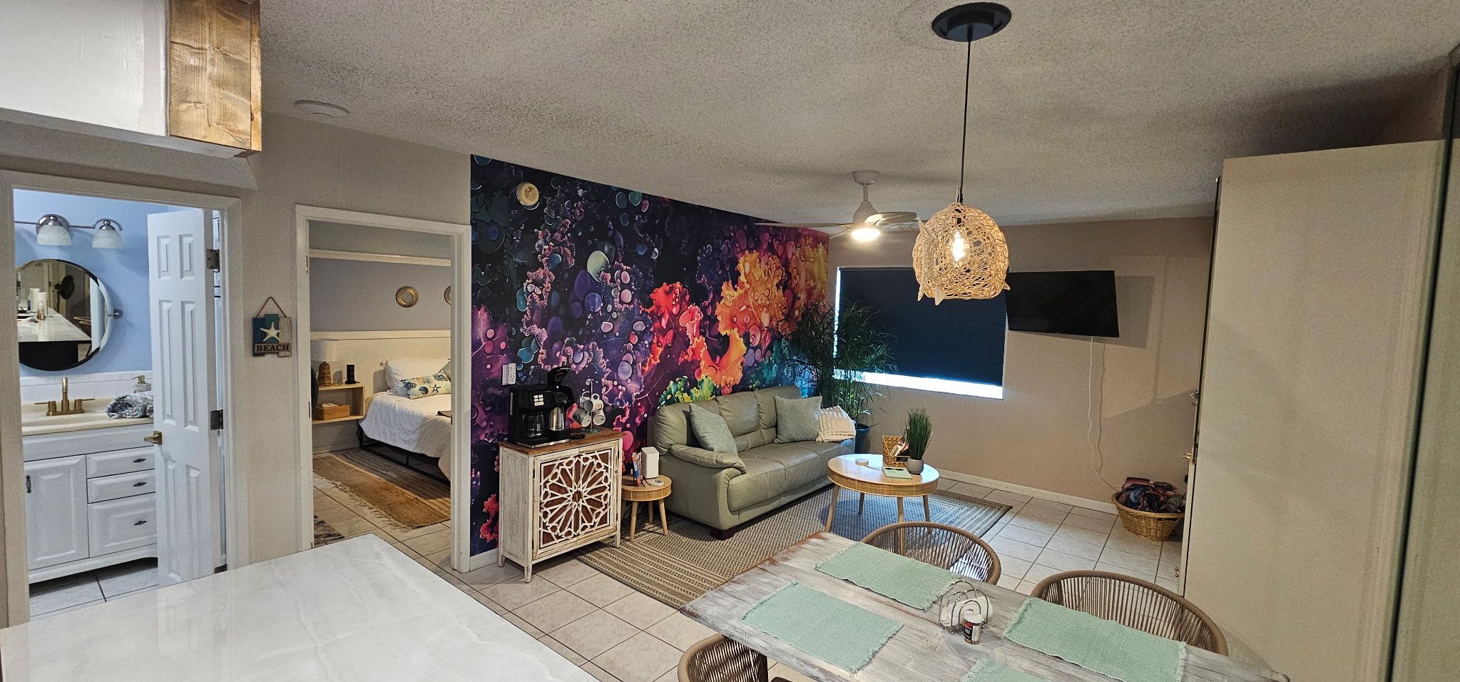 A living room with a colorful abstract mural, a sofa, a coffee table, and a dining area with chairs.