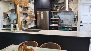 A kitchen with a central island, wooden cabinets, and a hanging light fixture. - Chic & Comfortable Beach Home • Walk/Bike to the Coast • All Essentials Included (Pompano Beach)