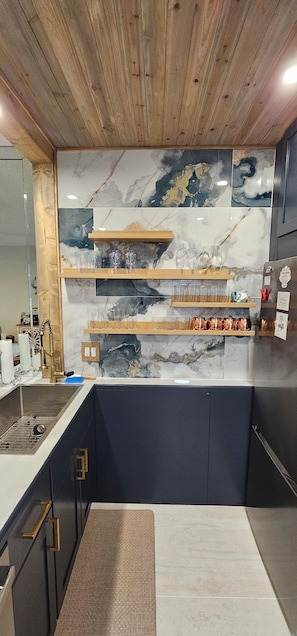 Eine Küche mit Marmorfliesenspiegel, Holzregalen und einem Edelstahl-Kühlschrank.