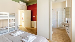 Habitación de hotel con literas, baño con lavamanos y toallero, y piso de madera.