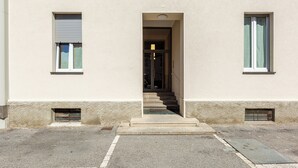 Un edificio con entrada central, una escalera y dos ventanas con persianas.