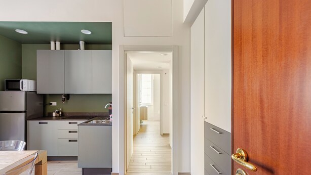 Una cocina moderna con gabinetes grises, una mesa de comedor de madera y vista a un pasillo que conduce a otra habitación.