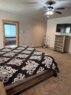 Une chambre à coucher avec un lit, un ventilateur de plafond, une télévision, une commode et une fenêtre.