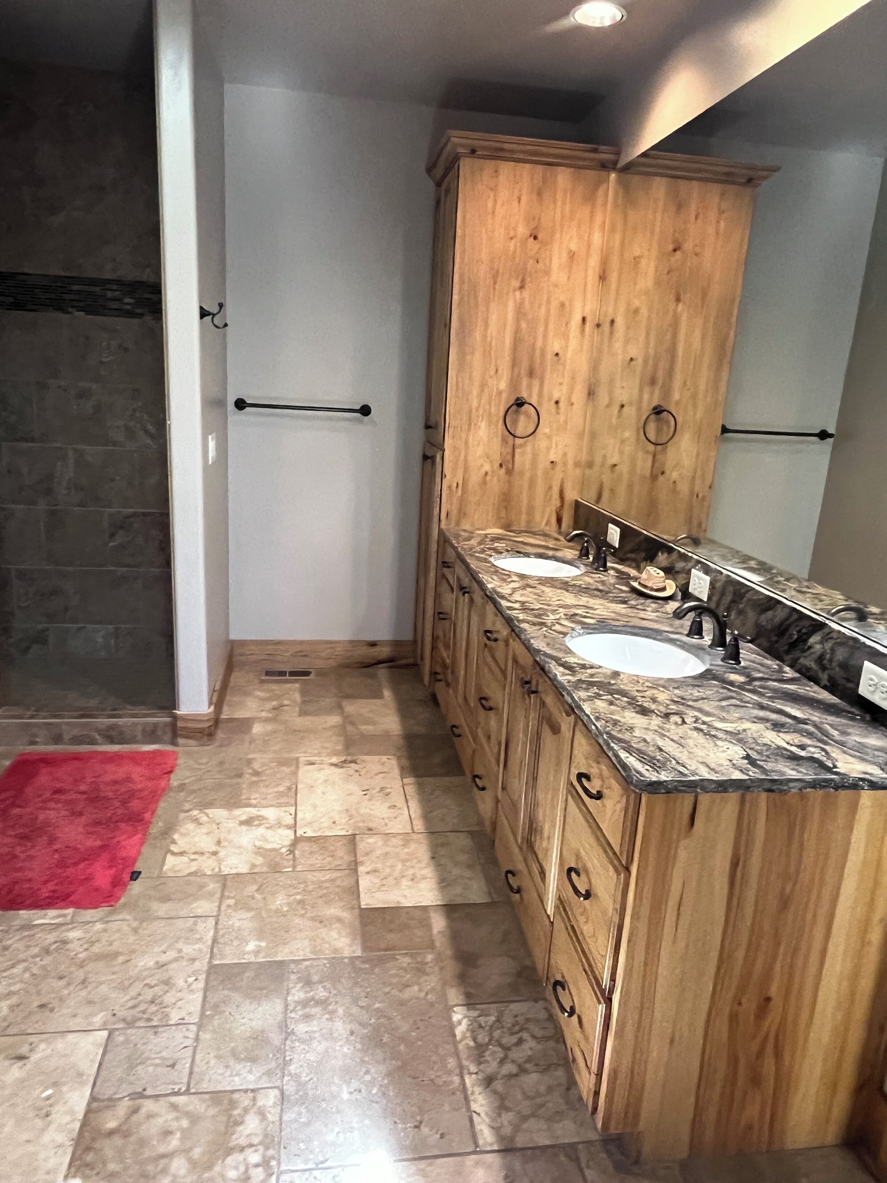 A bathroom with a wooden vanity, two sinks, and a shower area.