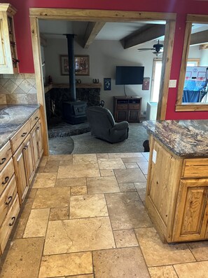 A kitchen with a stone floor, wooden cabinets, a stone fireplace, and a television mounted on the wall.