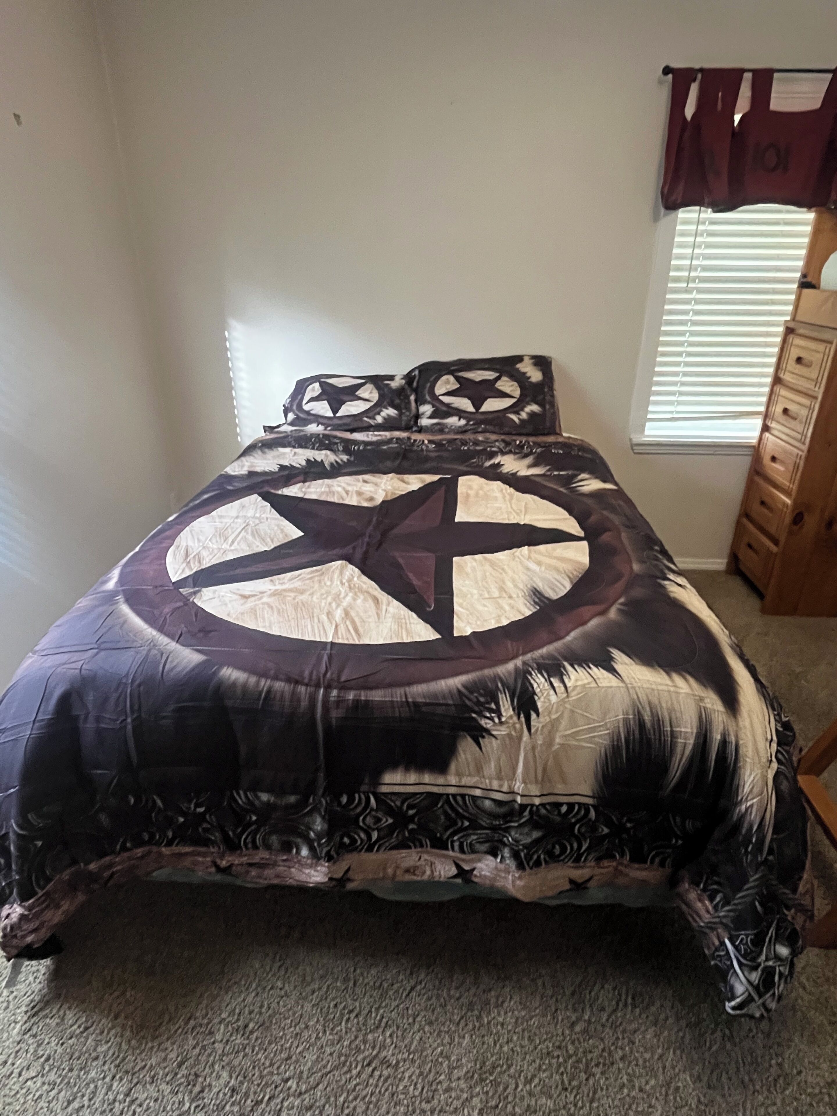 Una cama con una colcha estampada con motivos de estrellas, un aparador de madera y una ventana con persianas.