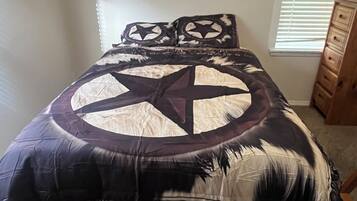 Una cama con una colcha estampada con motivos de estrellas, un aparador de madera y una ventana con persianas.
