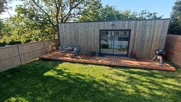 A backyard with a wooden deck, a barbecue grill, and a table with chairs.