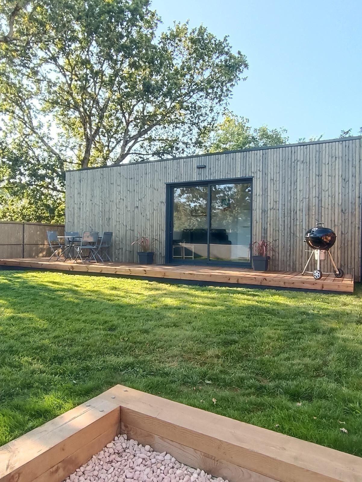 Une terrasse extérieure moderne, dotée d’une plateforme en bois, d’un barbecue et d’un espace détente avec des chaises.
