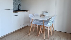 Cocina compacta con armarios blancos, un lavamanos integrado y una mesa de comedor blanca con cuatro sillas.