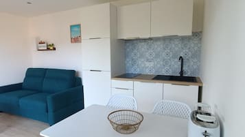 A compact living space with a kitchenette, a dining table, a sofa, and a toaster.