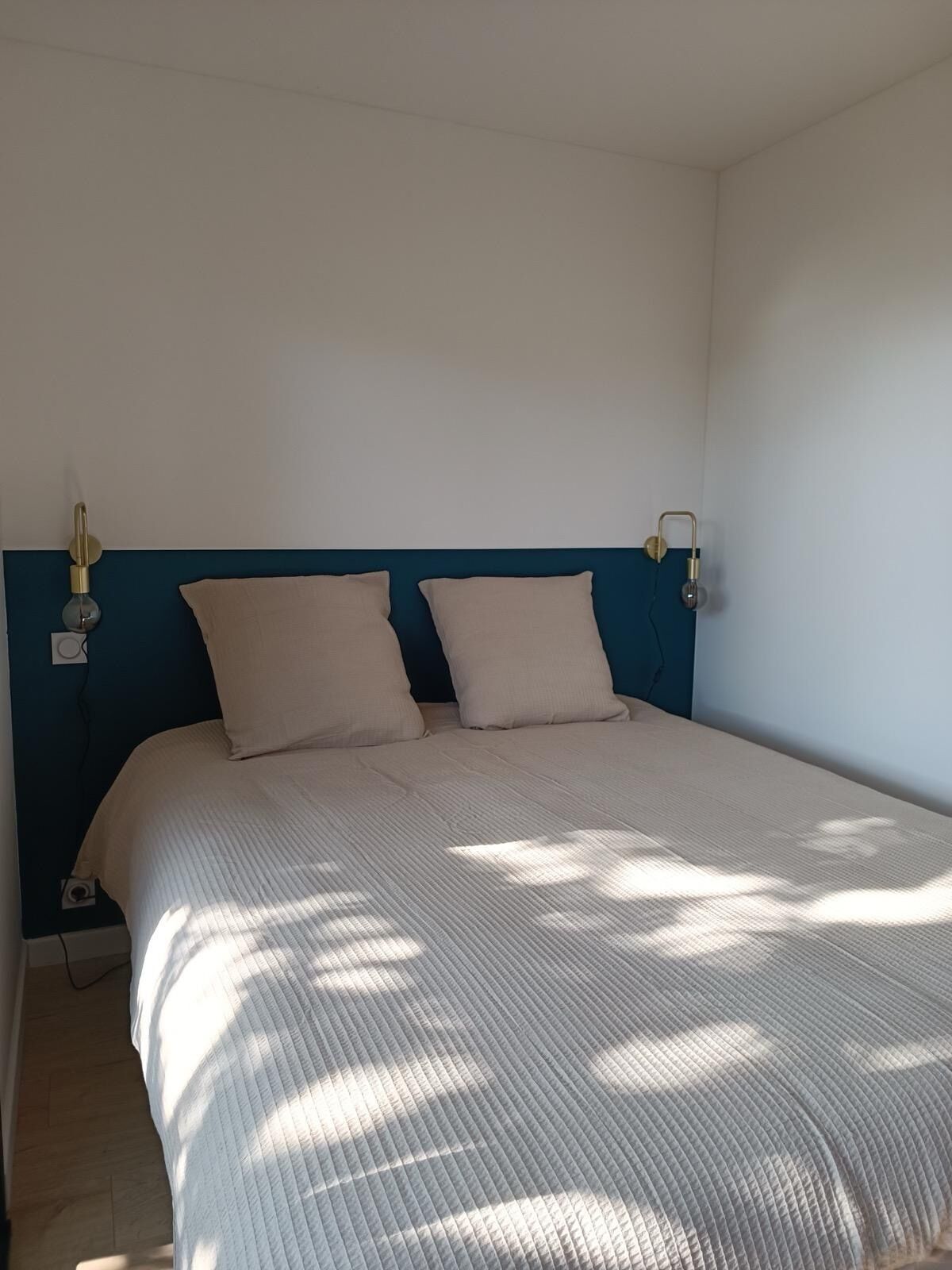A bed with a blue headboard, two beige pillows, and a white quilted bedspread.