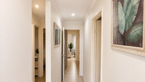 A hallway with a ceiling light, a framed botanical print on the wall, and a potted plant in the distance. - Modern Oasis | 3BR Home (Bassendean)