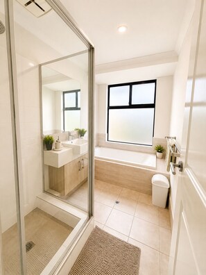 Ein modernes Badezimmer mit einer Duschkabine aus Glas, einer Badewanne, einem großen Fenster und einem Waschbecken.