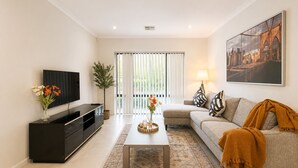 A living room with a TV, sofa, coffee table, and a painting on the wall. - Modern Oasis | 3BR Home (Bassendean)