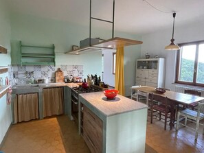 A kitchen with a central island, a dining area with a table and chairs, and a view of the outdoors through a window.