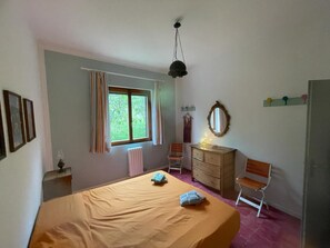 A bedroom with a bed, a dresser, a chair, a window, and a mirror.
