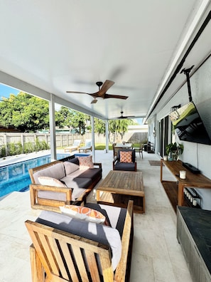 A covered outdoor area with a pool, wooden furniture, ceiling fans, and a barbecue grill. - Luxury beach house, heated pool, 10 minute walk to beach! (Pompano Beach)