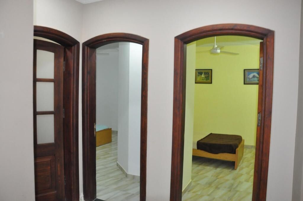 Un couloir avec une porte en bois, un mur recouvert de miroirs et une pièce comprenant un lit et un ventilateur de plafond.