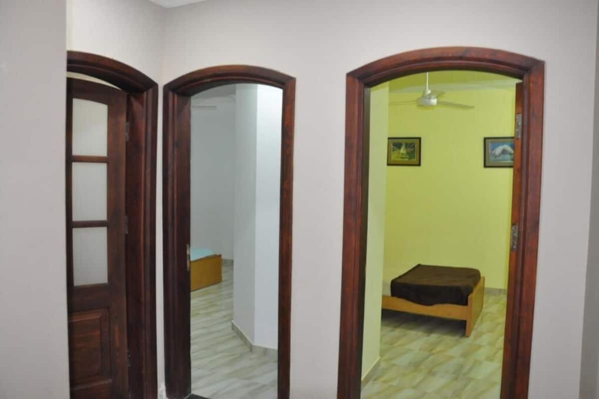 A hallway with a wooden door, a mirrored wall, and a room with a bed and a ceiling fan.