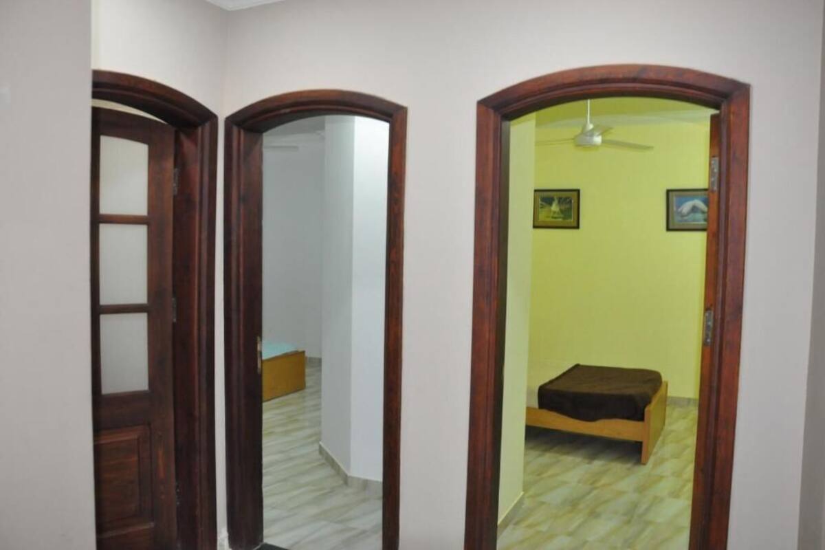 Un couloir avec une porte en bois, un mur recouvert de miroirs et une piĂšce comprenant un lit et un ventilateur de plafond.