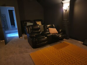 Ein wohnzimmer im dunklen Stil mit einer schwarzen Ledersofa, einem gelben Teppich mit Struktur und einer Tür zu einem anderen Raum.