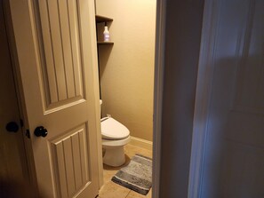Ein Badezimmer mit Toilette, einem Ablagefach mit einer Flasche und einer Tür.
