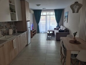 Ein modernes Wohnzimmer mit einer Couch, einem Couchtisch und einem Fernseher. Es gibt eine Küchenzeile mit Schränken und einem Spülbecken.