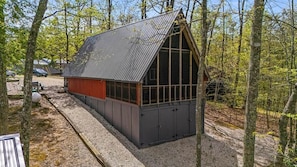 A cabin with a sloped roof, large windows, and a gravel driveway.