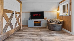 Ett mysigt vardagsrum med en platt-TV som visar "NETFLIX", en vägg med träram, en grå soffa med mönstrade kuddar och en inbyggd mediabänk.