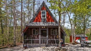 A cabin with a triangular roof, large windows, and a door, surrounded by trees.