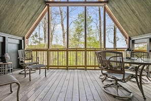 A covered outdoor area with a table and chairs, a view of trees through the railing, and a wooden floor.