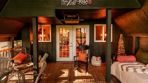 A cozy room with a wooden ceiling, a bed, a rocking chair, a small table, and a Christmas tree.