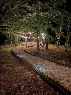 Ein Sitzbereich im Freien bei Nacht mit Lichterketten, einem Feuerkorb und einer Hängematte.