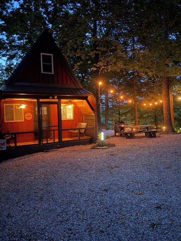 Una cabaña de madera con un porche, una mesa de picnic y luces colgantes.