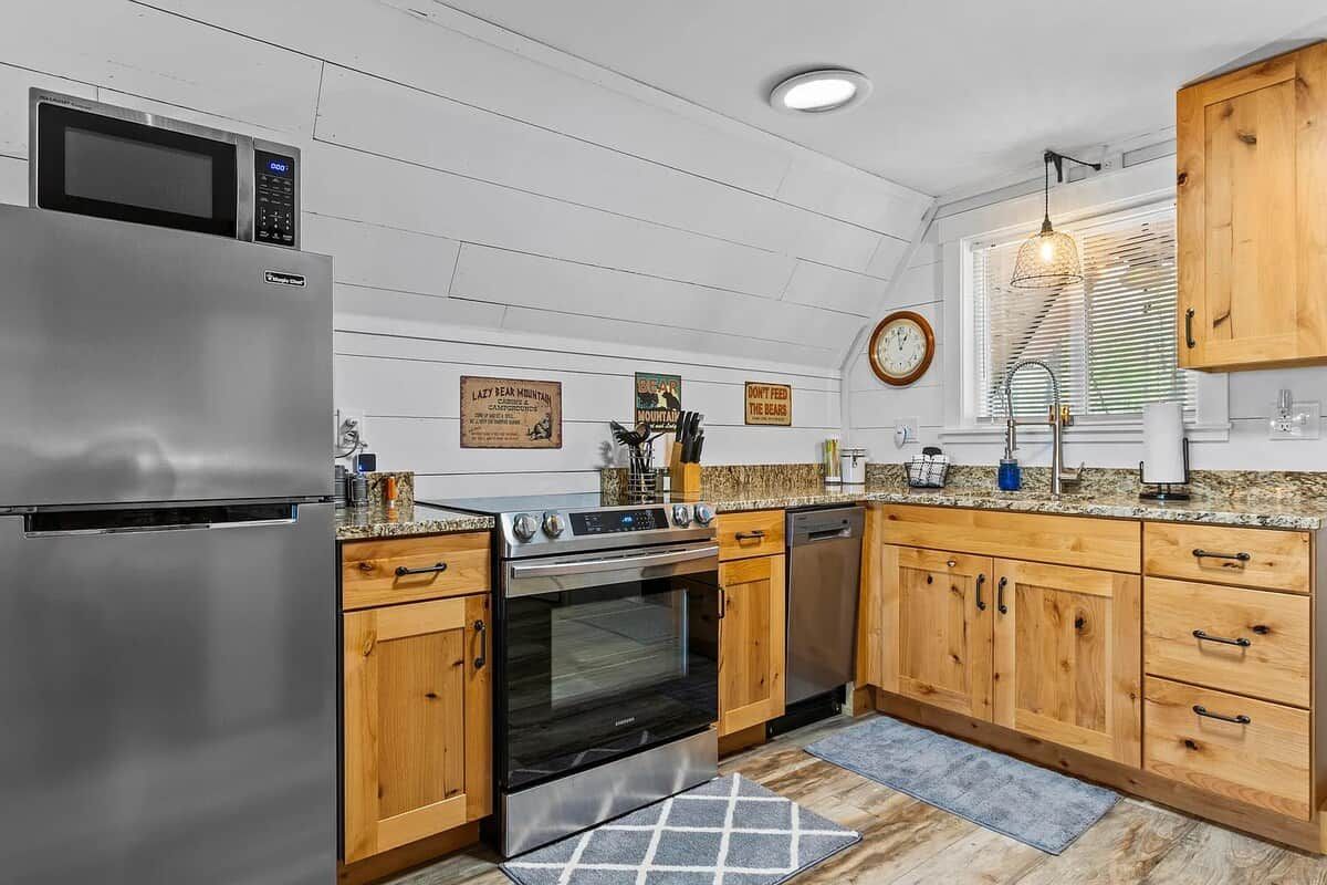 A kitchen with a stainless steel refrigerator, oven, and dishwasher, wooden cabinets, and a window with blinds.