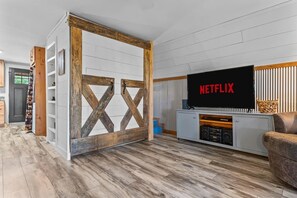 Ein Wohnzimmer mit Fernseher, auf dem 'NETFLIX' angezeigt wird, einem Holzkasten und einem Sofa.