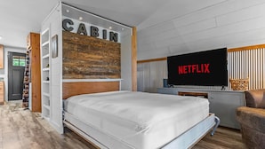 Ett modernt sovrum med en säng, en tv som visar Netflix och en skylt med texten ”CABIN” ovanför sängen.