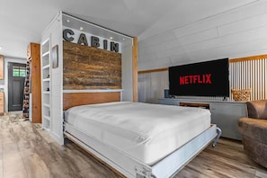 Une chambre moderne avec un lit, un téléviseur affichant le logo « NETFLIX », et une pancarte « CABIN » au-dessus du lit.
