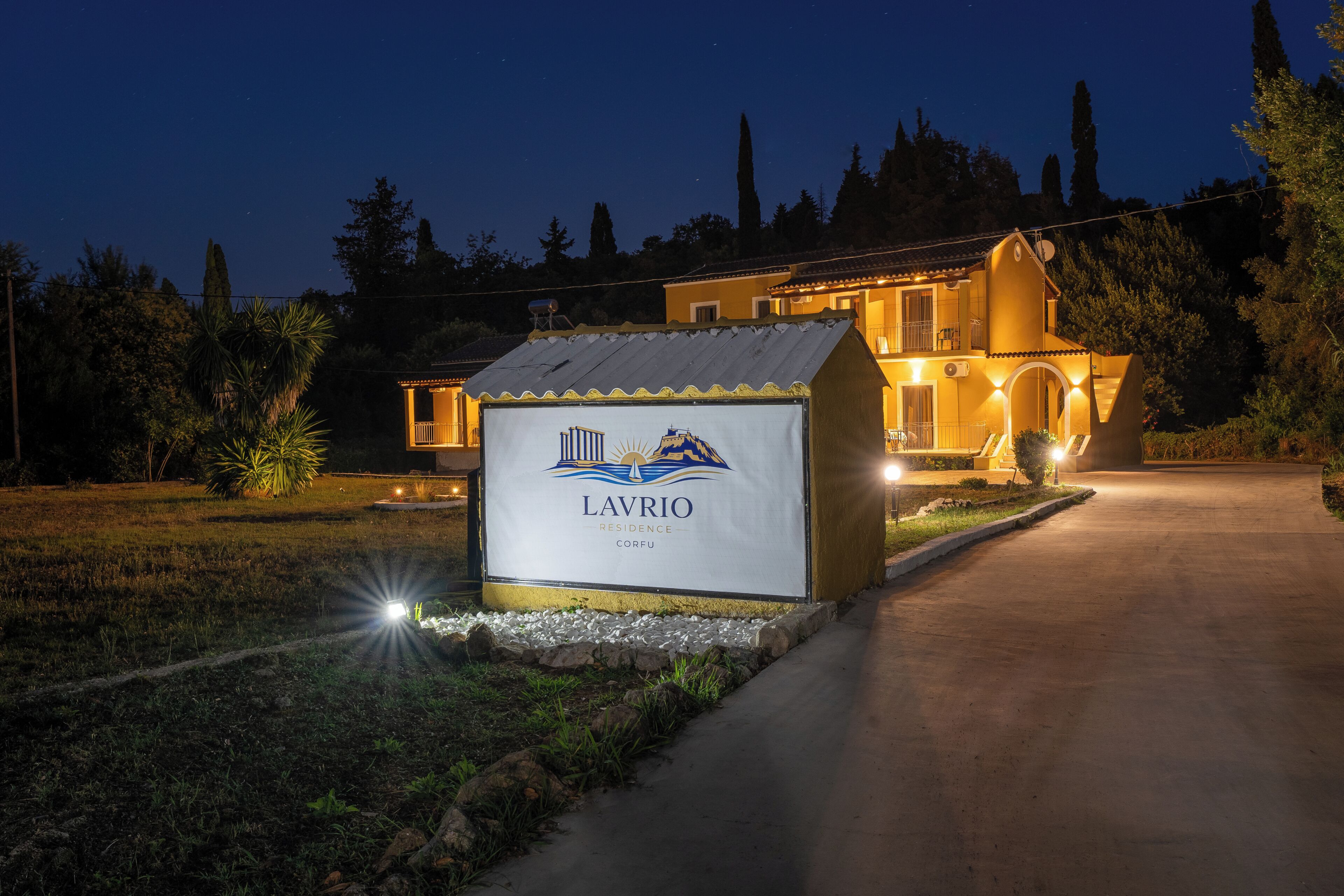 A residential property named Lavrio with a well-lit entrance and a pathway leading to the main building.