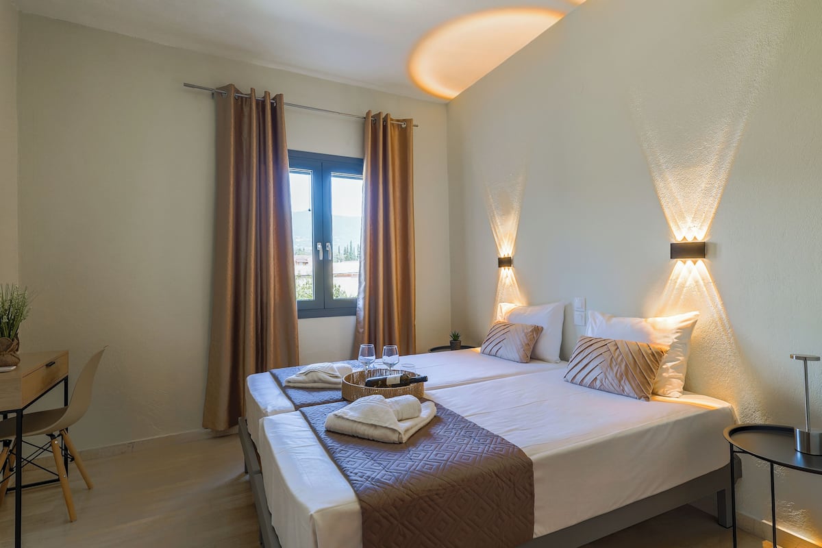 Habitación de hotel con cama, mesita de noche, lámpara, cortinas y vistas al exterior.
