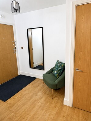 Ein Zimmer mit Holzboden, einem grünen Sessel mit gemustertem Kissen, einem großen Spiegel an der Wand und einer Holztür.