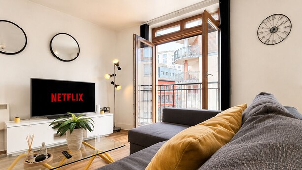 Un soggiorno moderno con TV a schermo piatto, divano, tavolino da caffè e una grande finestra con vista sugli edifici.