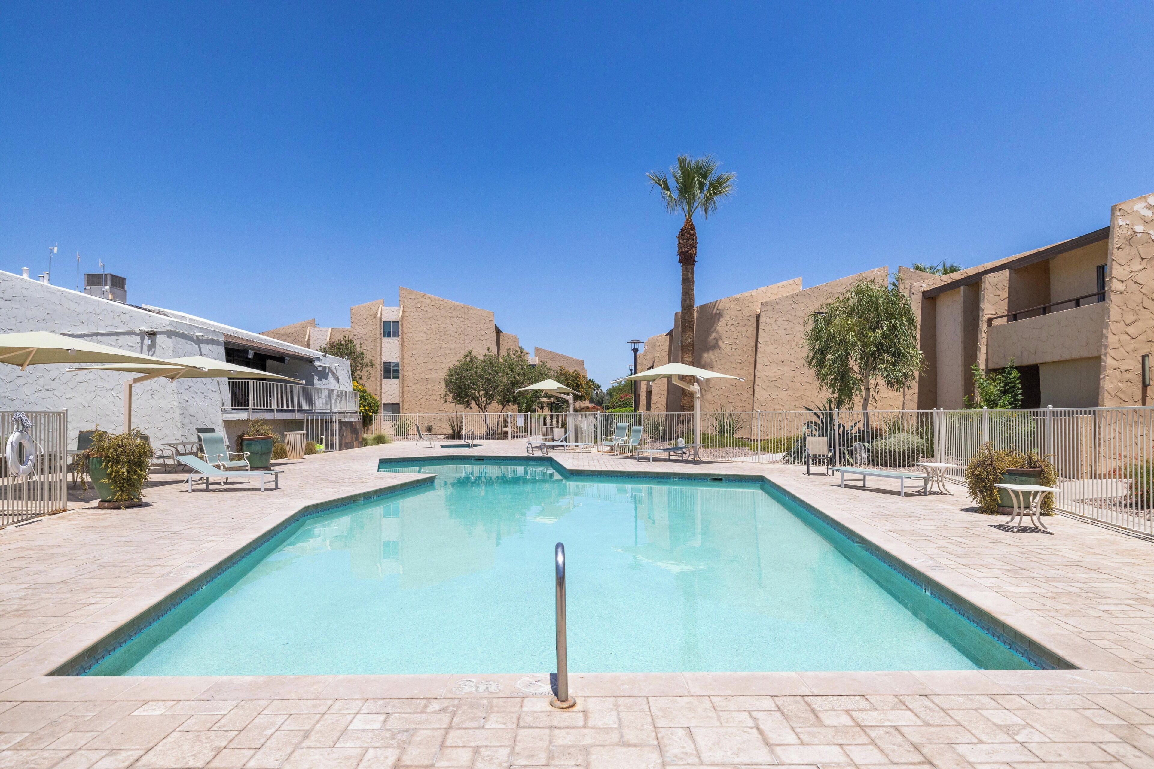 A swimming pool with lounge chairs and umbrellas, surrounded by buildings with a modern design.